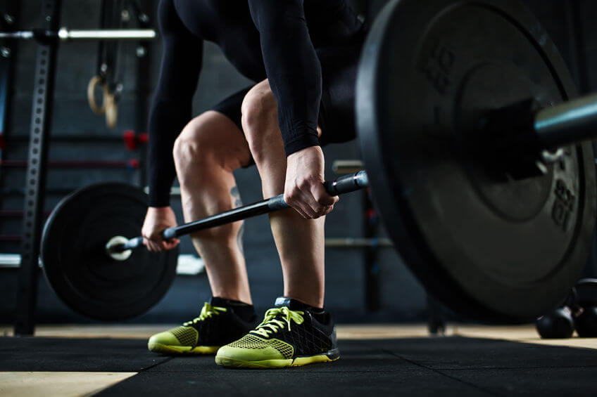 Active young man training with barbell in gym