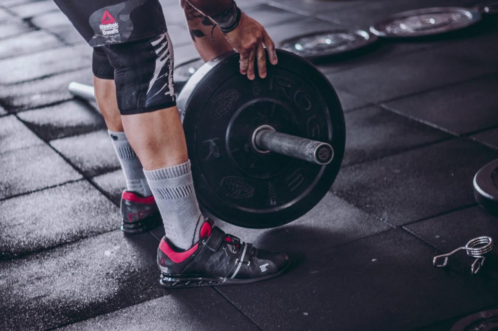 man with knee sleeves picks up barbell