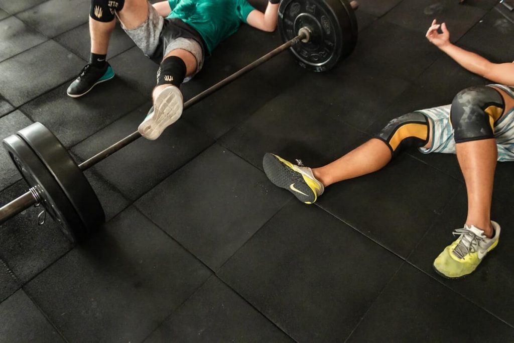 two men lying on CrossFit gym floor beside Olympic barbell