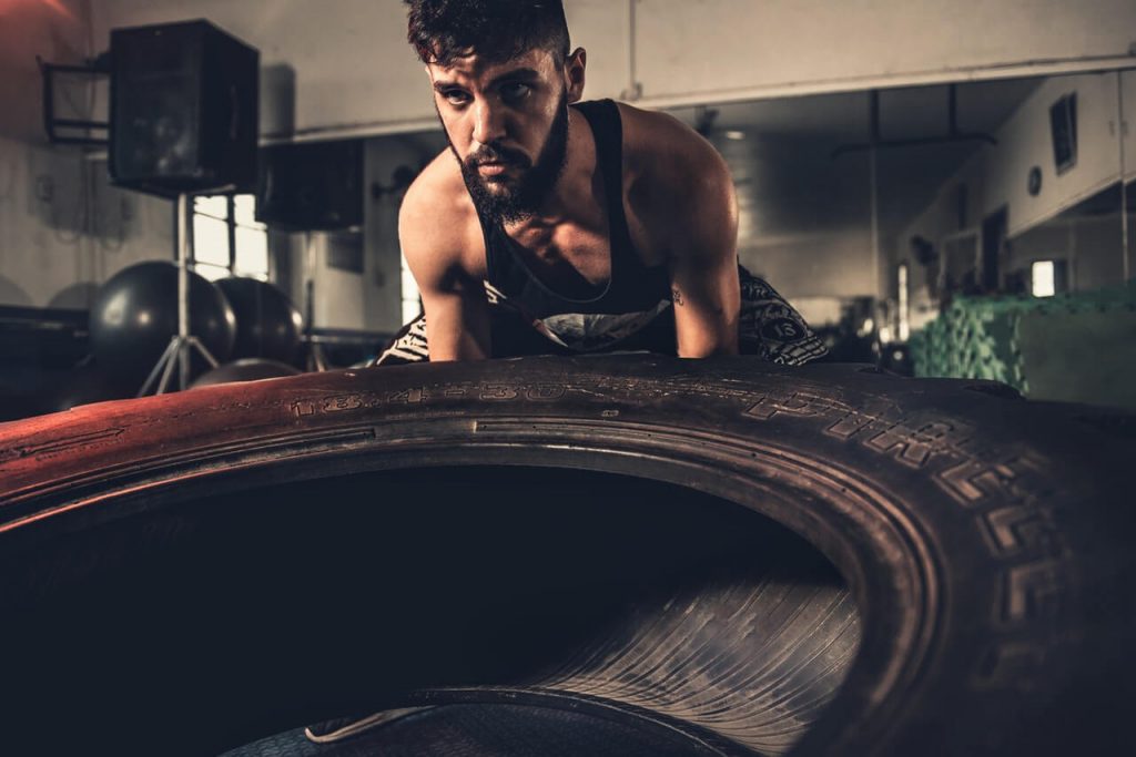 man lifting vehicle tire in gym