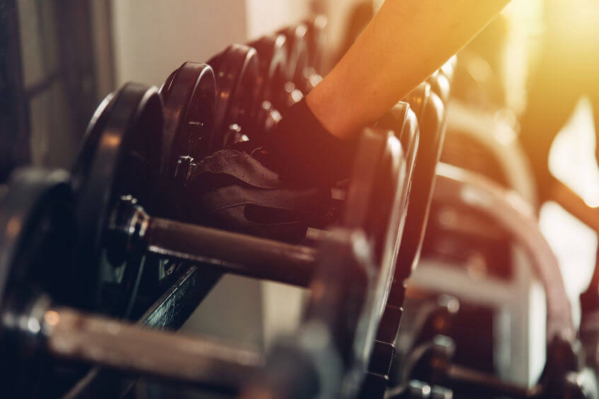 woman wearing weight lifting gloves holding dumbbell at gym