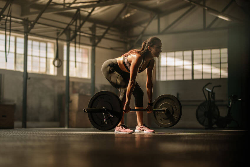 female athlete performing weight lifting exercise at gym