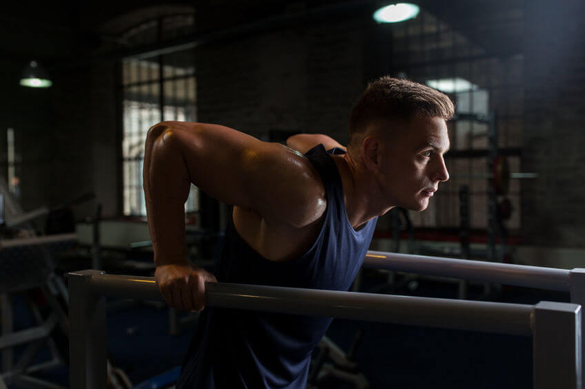 man doing triceps dip on parallel bars in gym