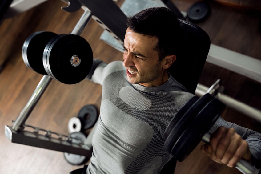 man holding dumbbells and working bench press at gym