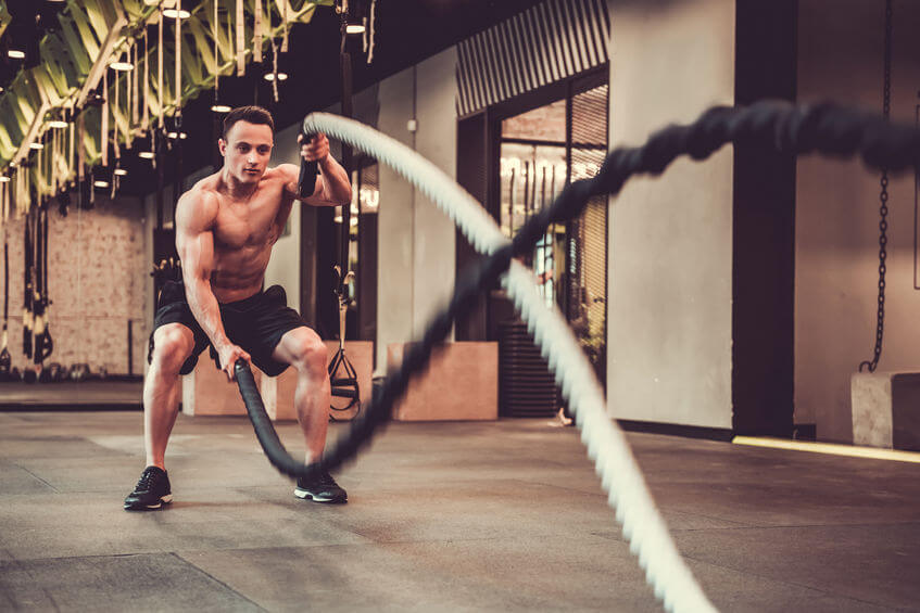 muscular man is doing battle rope exercise