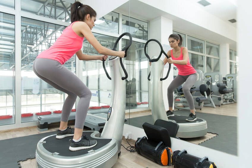 young woman training with whole body vibration machine in the gym