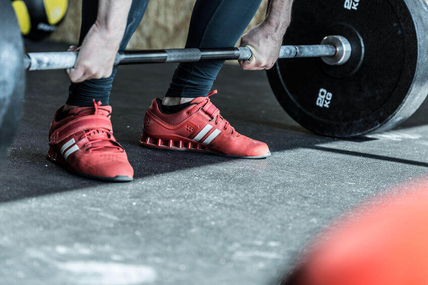 man wearing weightlifting shoes and lifting heavy barbell