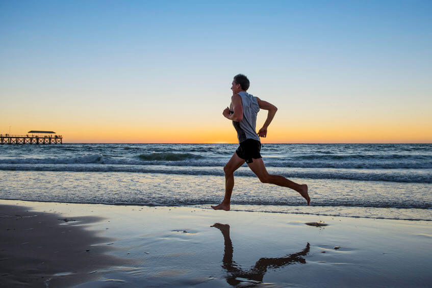 runner man training on sunset beach running barefoot