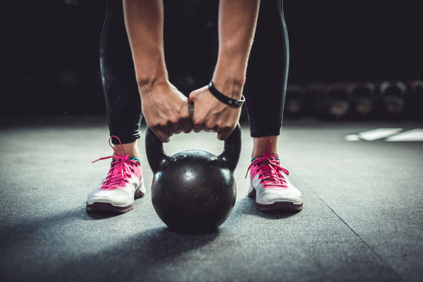 woman in CrossFit gym holding a kettlebell and wearing CrossFit shoes