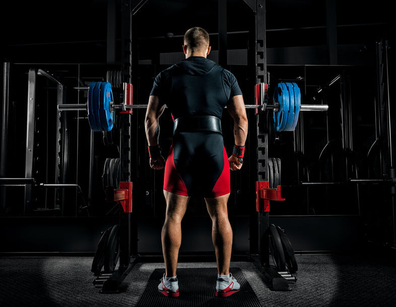 athlete stands in front of the power rack with a barbell