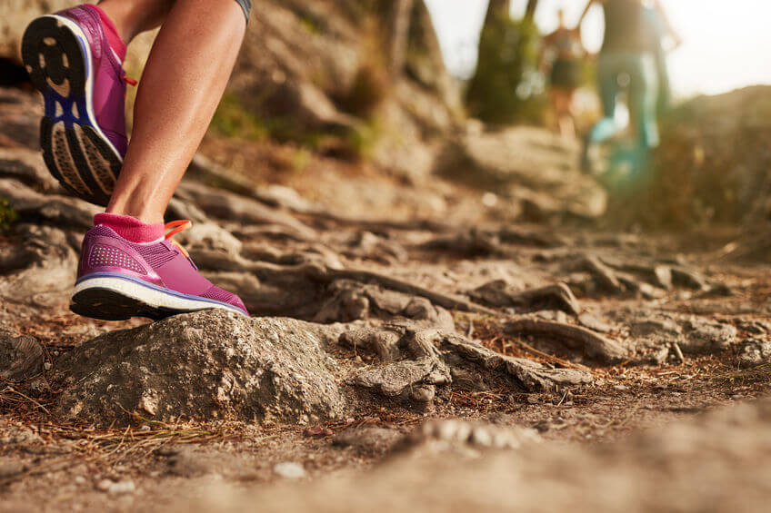 close up of an women's feet wearing trail running shoes on rocky terrain trail