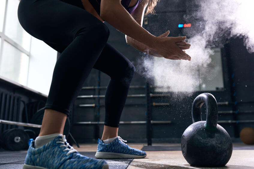 woman rubbing hands with gym chalk preparing to lift kettlebells