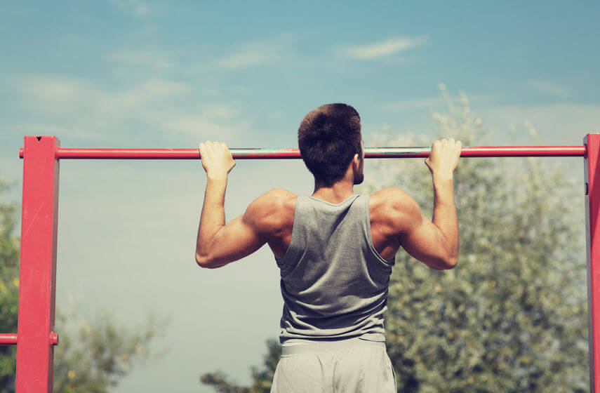 young man doing pull ups on horizontal bar outdoors