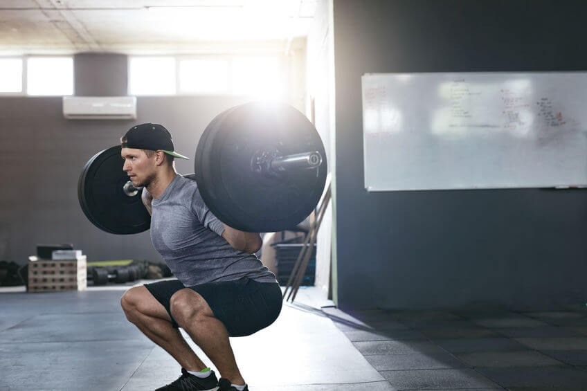 man doing squats with barbell at the gym