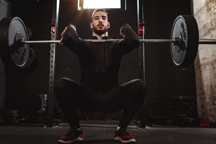 man is doing squat exercise with barbell at the gym