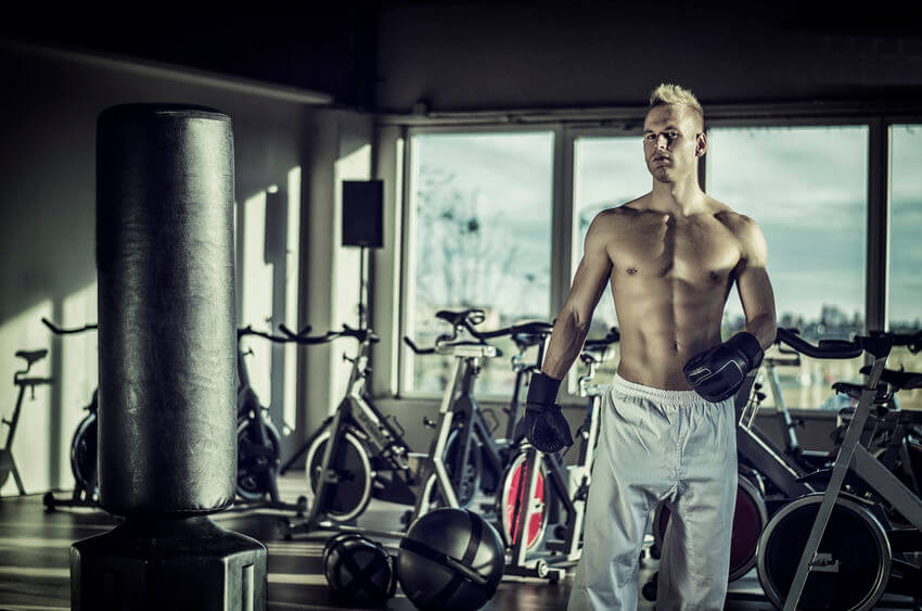 man with boxing gloves hitting free-standing punching bag at the gym