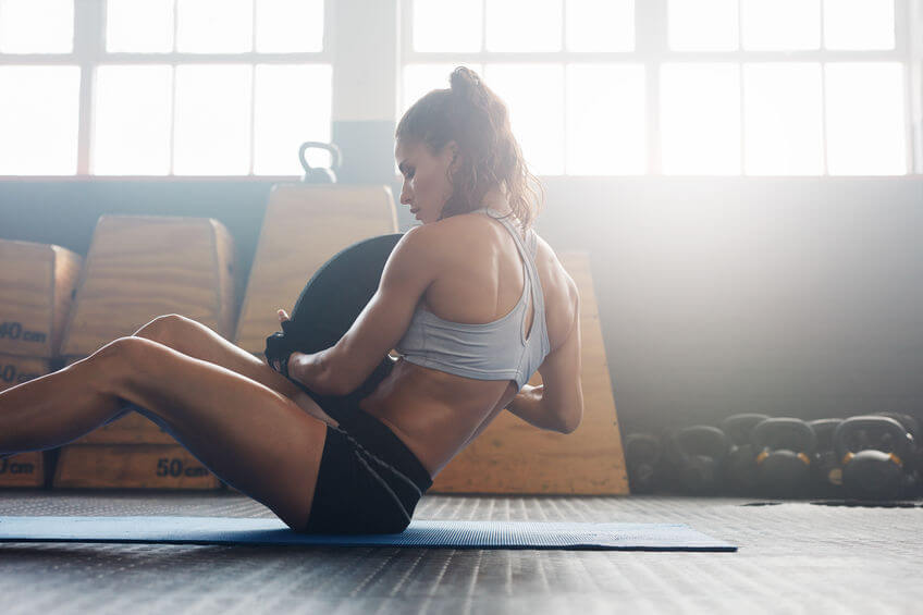 woman doing sit ups with holding a weight plate and wearing gloves